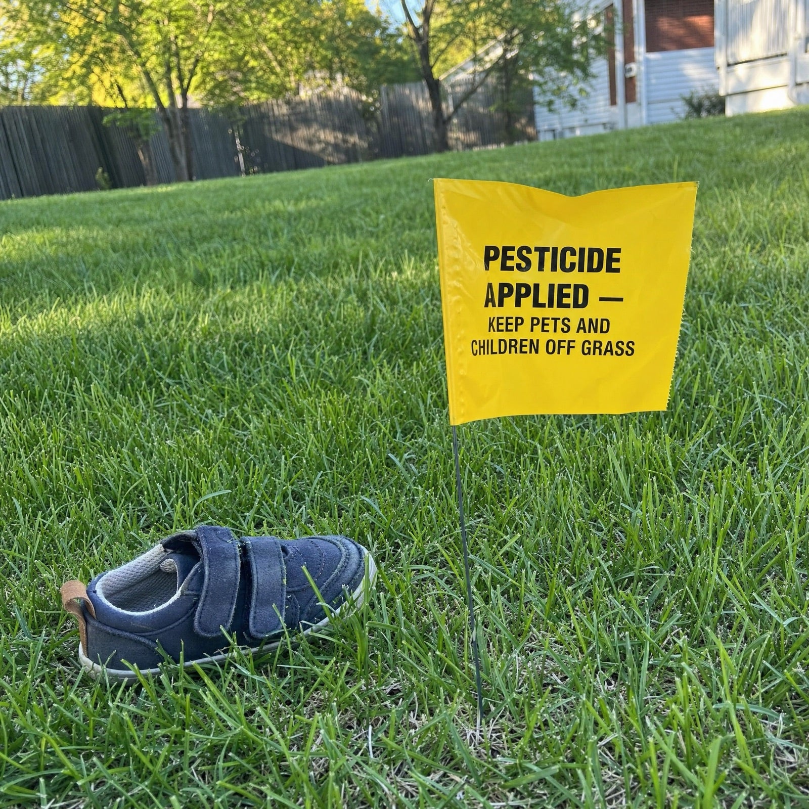 A 'pesticide applied — keep pets and children off grass' flag staked in a green lawn beside a child's shoe.